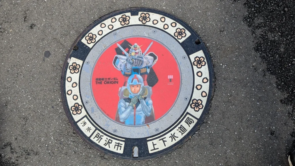 Manhole cover in Tokorozawa featuring Mobile Suit Gundam THE ORIGIN, with a cherry blossom ring
