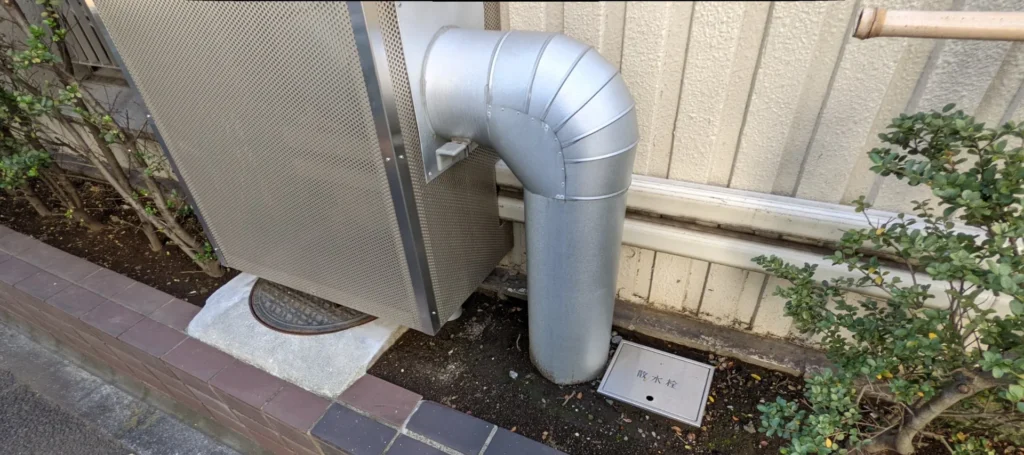A manhole cover half-hidden under a large metal equipment box, next to a small sprinkler tap lid