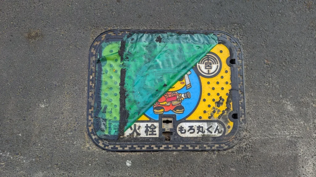 Fire hydrant cover with the mascot Moromaru-kun, partly covered by a peeling green sheet