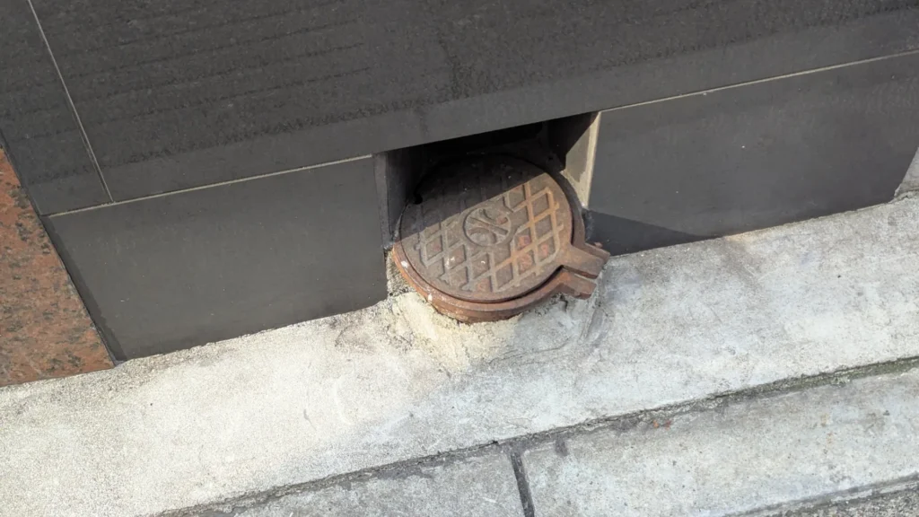 A small round lid tucked into a gap at the bottom of a building wall