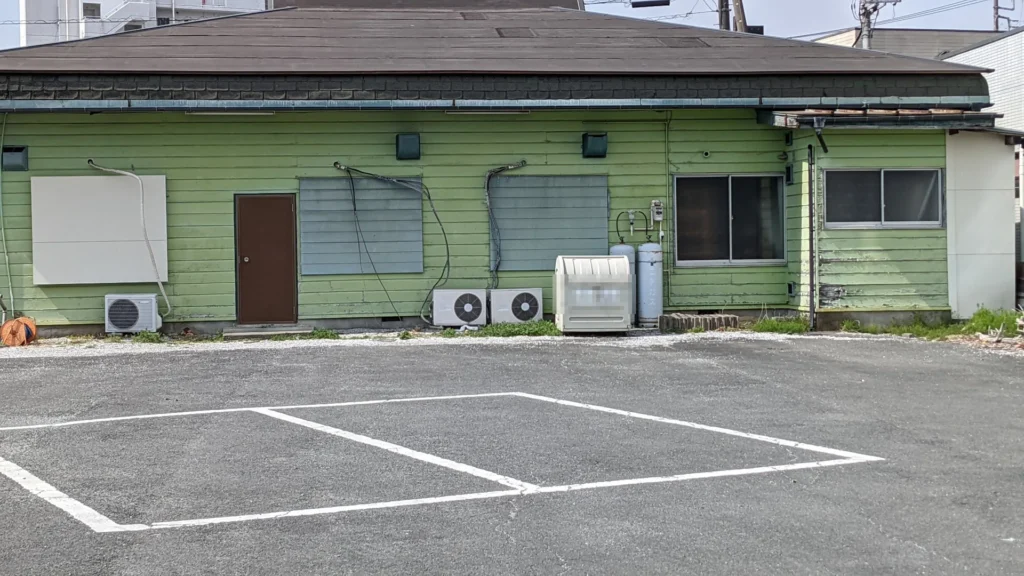 Outdoor air conditioner units lined up behind an old green wooden building