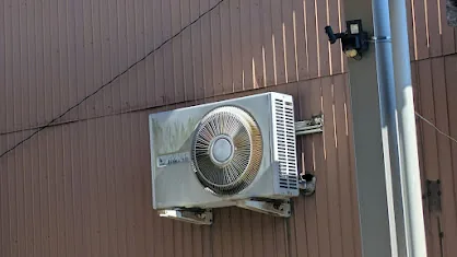 A right-eye outdoor unit mounted high on a brown corrugated metal wall